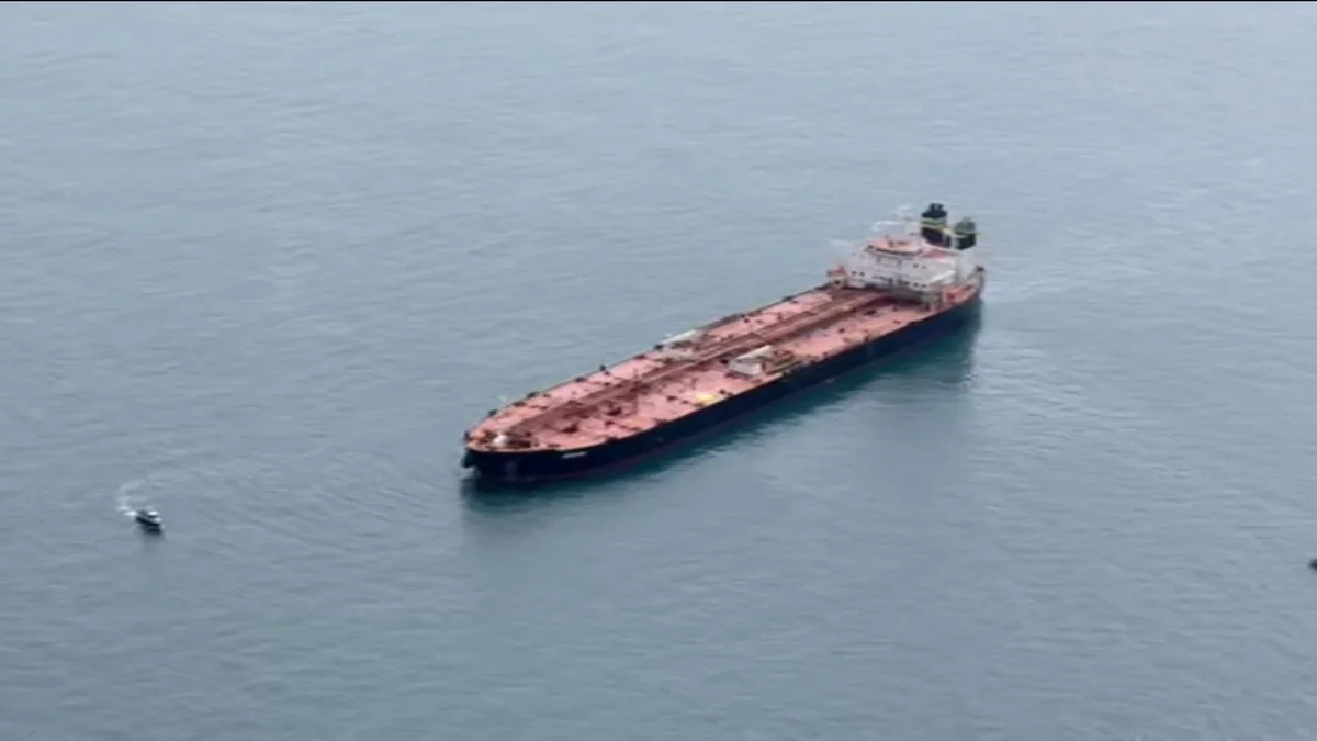 Большой нефтяной танкер с красной палубой в открытом море рядом с маленькой лодкой