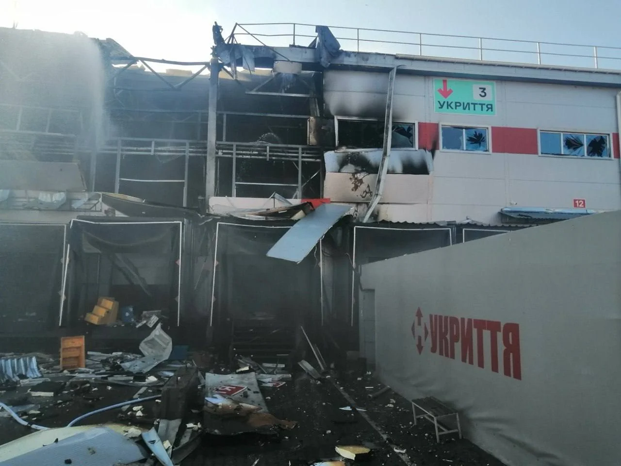 Разрушенный терминал с дымом, обломками и вывесками «Укрытие» после удара
