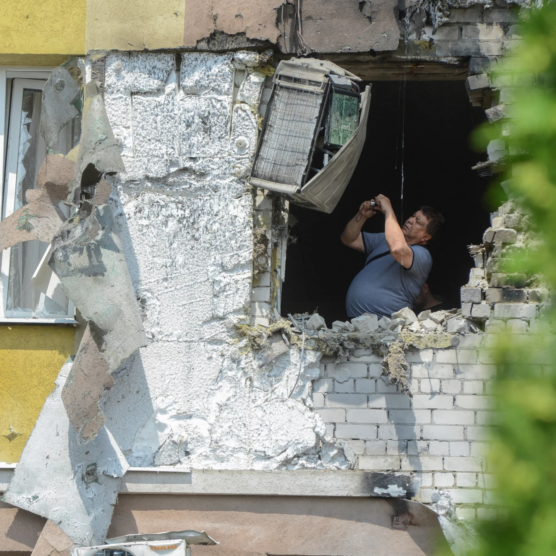 Чоловік оглядає зруйновану стіну будинку з висячим кондиціонером