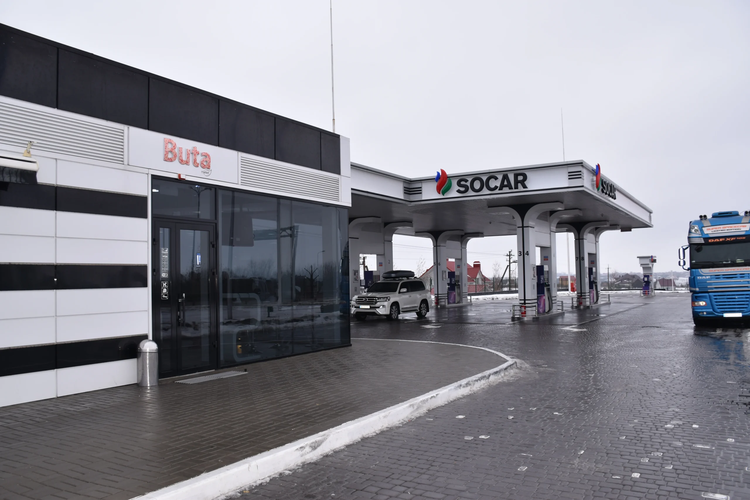 АЗС SOCAR з білим позашляховиком і синьою вантажівкою на мокрій площі